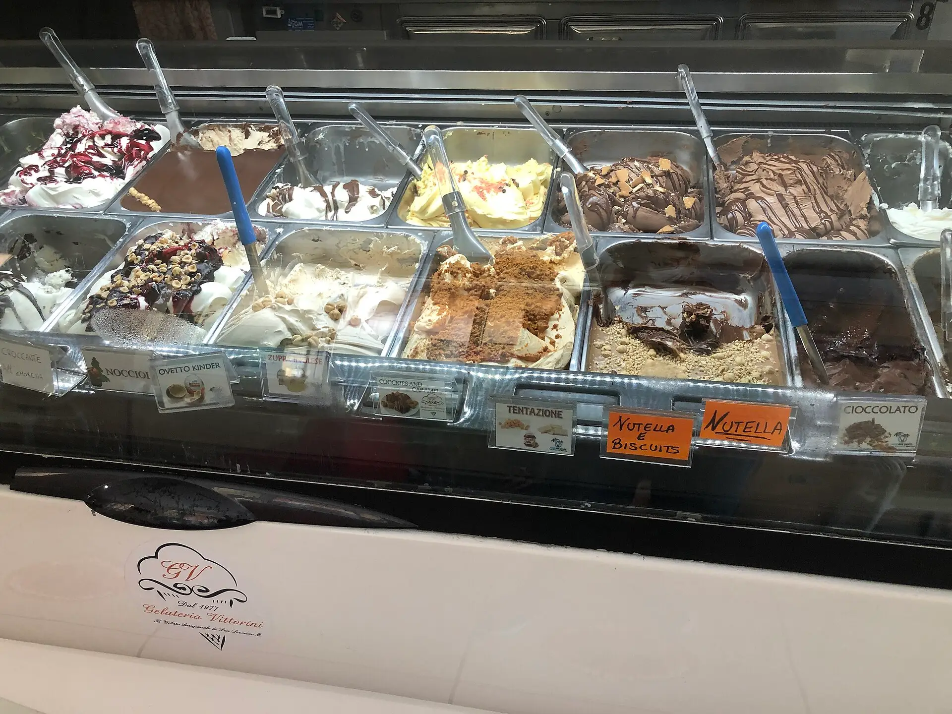 An Italian gelateria display case — rows of flavours under glass, including Nutella, pistachio and stracciatella.