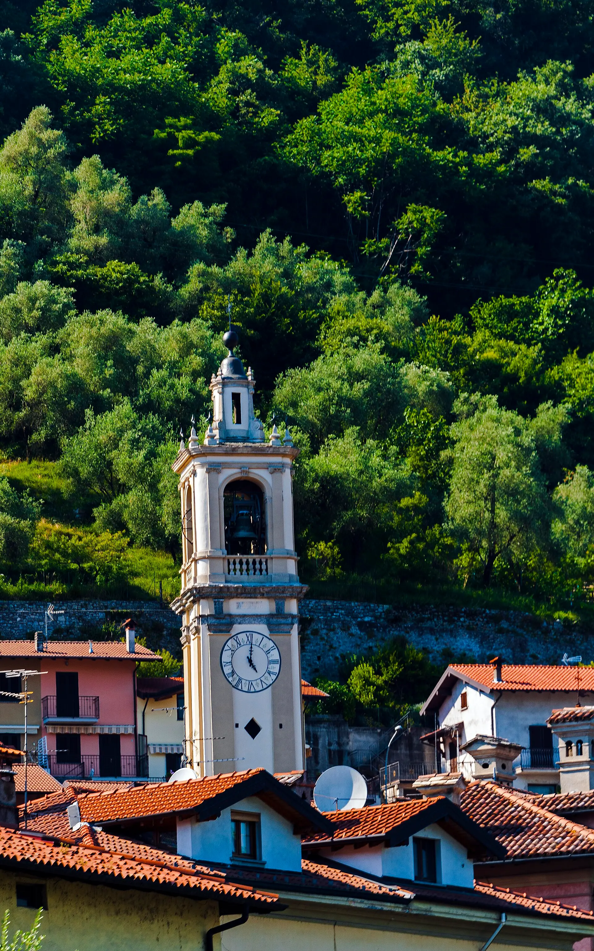 A baroque village bell tower rising above the red roofs of a Lake Como village — the Greenway winds through small lakeside hamlets like this one.