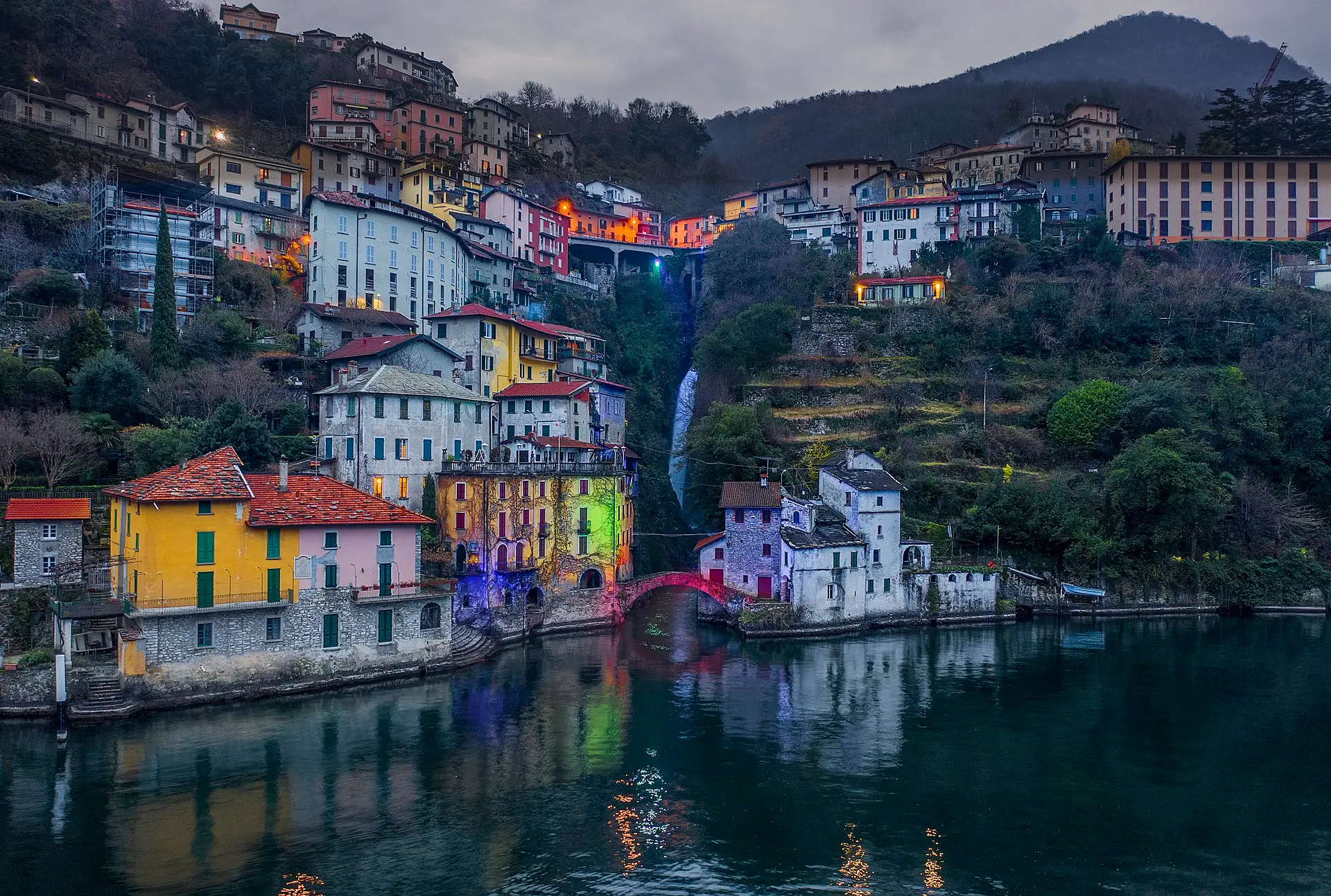 Nesso, Lake Como — colourful houses cascading down to the lake around the village's natural cove, illuminated in the evening light.
