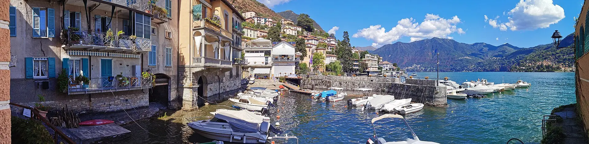 Moltrasio harbour on Lake Como — colourful lakeside buildings, small fishing boats, and the mountains across the water.